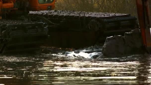 Eine breite Schaufel des Baggers gräbt bei Sonnenuntergang das Erdreich vom Grund des Flusses. Reinigung und Vertiefung des Kanals. — Stockvideo