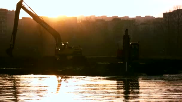 Las excavadoras limpian y profundizan el lecho del río al atardecer . — Vídeo de stock