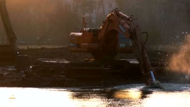 Grävmaskiner rengör och fördjupar flodbädden vid solnedgången. — Stockvideo