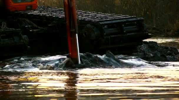 Un large seau d'excavatrice récupère le sol du fond de la rivière au coucher du soleil. Nettoyage et approfondissement du canal .