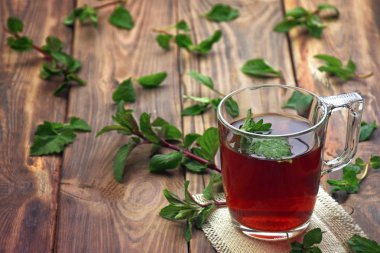 Taze nane nane ile süslenmiş cam, bitkisel çay yaprakları hazırlanmış. Seçici odak. Eski bir ahşap zemin üzerine bir fincan güzel kokulu bir içki.