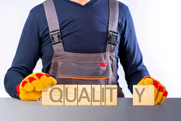 The concept of high quality construction. Builder in overalls points to a wooden board with the text: QUALITY.