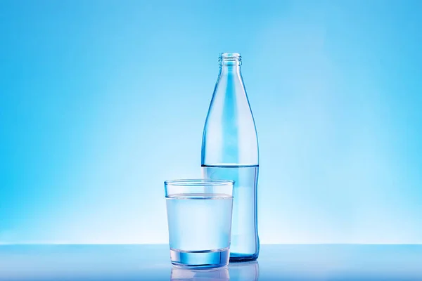 Clear mineral water bottle and glass on blue background with copy space.