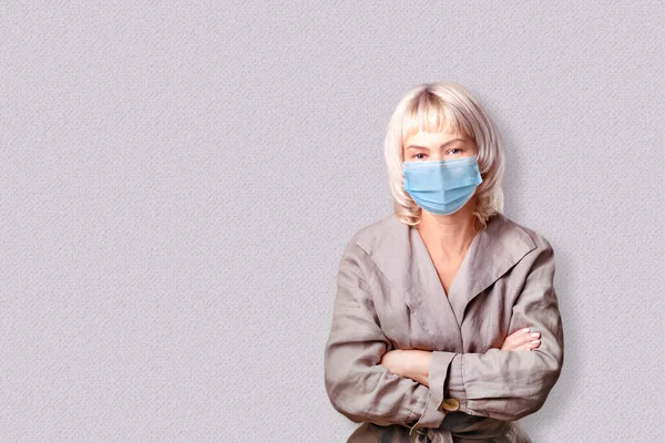 Business woman fears the virus and wears a face mask on grey background with copy space.