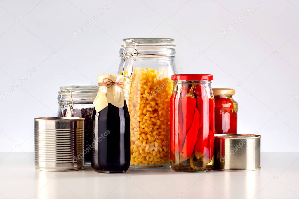Different glass jars with grains, pasta, vegetable, cans of canned food on the table.