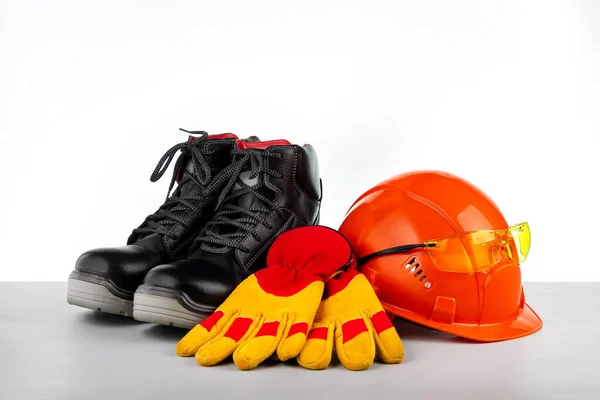 Protective hard hat, boots, gloves and glasses on grey surface.