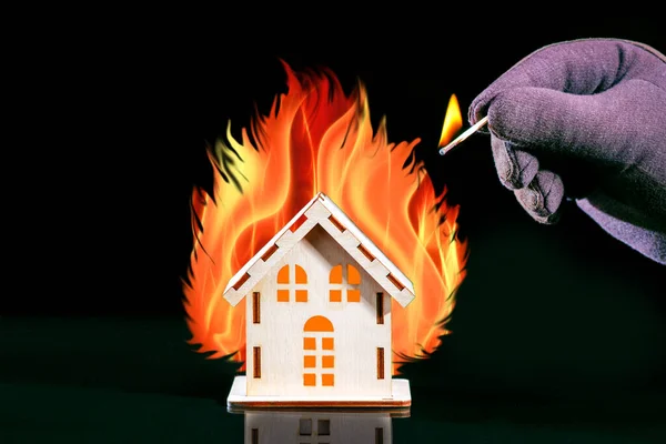 House With A Big Fire. Hand with a burning match sets fire to the house model. Fire safety concept.
