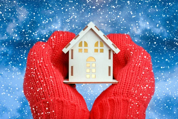 Eldivenli eller kar yağışı arka planında model evi tutuyor. Ev Enerjisi Verimliliği Konsepti. Sıcak ev.