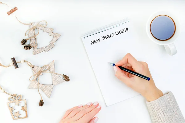 Woman hands in sweater is writing goals in a notebook for New Year. Planning concept.