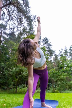 Kadın parkta üçgen yoga pozu veriyor. Esneklik ve çekirdek gücü için açık havada esneme hareketleri. Aktif sağlıklı yaşam tarzı konsepti. Yüksek kalite fotoğraf