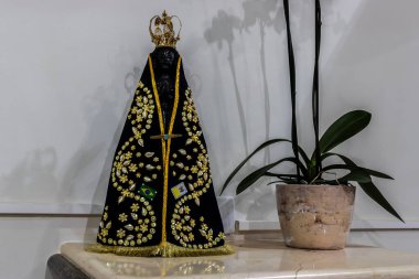 Image of Our Lady Aparecida, patron saint of Brazil, with a black mantle, gold details and flags.