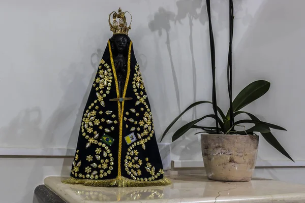 Image of Our Lady Aparecida, patron saint of Brazil, with a black mantle, gold details and flags.
