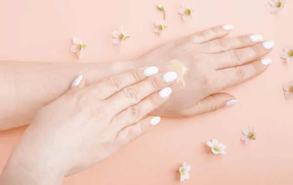 hands with cream on a pink background with white flowers close-up. middle age skin care product, beauty, hand care, spa.