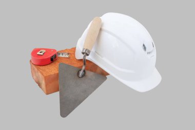 Tuğla, miğfer, mezura ve gri arka planda spatula. Kesme Yolu