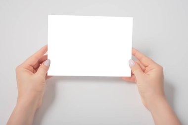 Kadın eli, gri kağıt üzerinde boş bir çarşaf tutuyor. Boş bir kağıt parçasının maketi