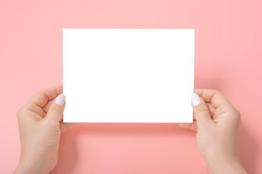 Pembe üzerinde boş bir kağıt çarşaf tutan kadınların elleri. Boş bir kağıt parçasının maketi