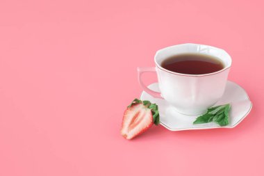 Çilekli ve naneli çay. Nane yaprakları ve olgun çileklerle dolu beyaz bir fincan çay. pembe arka plan. kopyalama alanı.