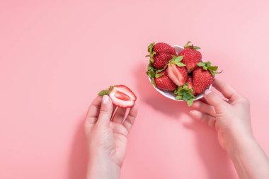 Yakın plan, pembe arka planda beyaz kasede soyulmuş taze çilek. Bir kadının eli kaseden çilek alır Sağlıklı beslenme kavramı.