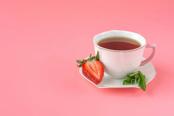 white cup of tea with mint and red ripe strawberries on pink background. top view. close-up