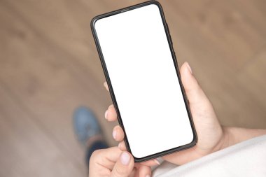 Üst görüntüde, elinde siyah bir cep telefonu olan beyaz ekranlı bir kadın resmi var. Ahşap zemin arkaplanı.