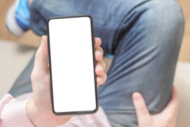 Görüntü görüntüsü boş beyaz ekran cep telefonu. Evdeki koltukta cep telefonuyla mesajlaşan bir adam. Reklam metni için boş alan. Kot pantolonlu genç adam akıllı telefon ekranına bakıyor evdeki kanepede oturuyor. İnsanlar pazarlama sektörü ve teknolojiyle iletişime geçiyor