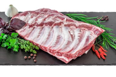 Çiğ domuz kaburgası ve baharatlar siyah bir kesme tahtasına serilmiş. Koyu siyah arka planda baharatlı çiğ domuz pirzolası. Çiğ domuz pirzolası, biber, fesleğen ve sarımsak.