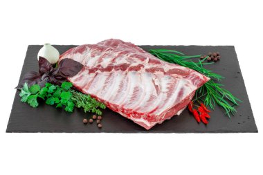 Çiğ domuz kaburgası ve baharatlar siyah bir taş kesme tahtasına serilmiş. Koyu siyah arka planda baharatlı çiğ domuz pirzolası. Çiğ domuz pirzolası, biber, fesleğen, sarımsak ve sos.