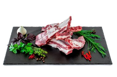 Taş kesme tahtasının üzerinde taze bitkilerle çiğ domuz pirzolası. Çiğ domuz kaburgası taze bitkiler ve baharatlarla siyah bir taş kesme tahtasına serilmiş..