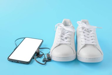 Spor ayakkabı ve telefon. Boş ekranlı cep telefonu, mavi arka planda beyaz spor ayakkabılar. Boş Moblie akıllı telefonu, kulaklıkları ve spor ayakkabıları var.