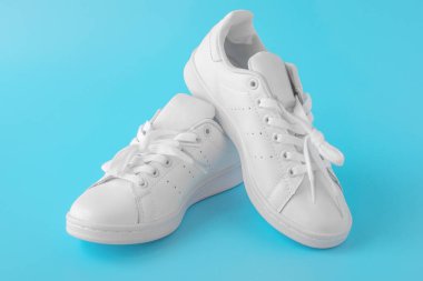 Mavi arka planda bir çift yeni beyaz spor ayakkabı. Yeni beyaz deri spor ayakkabılar. Koşu, tenis, koşu için spor ayakkabıları.