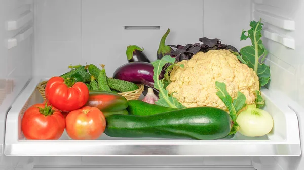 Shelf in the refrigerator with vegetables. Open refrigerator full of vegetables. healthy food. healthy lifestyle concept. Fresh vegetables in refrigerator. On the shelf tomato, eggplant, cauliflower, onions, zucchini and other vegetables.