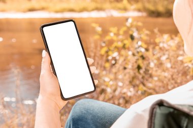 Sonbaharda geçmişi bulanık, akıllı telefon tutan bir kadın. Açık hava parkında cep telefonu kullanan bir kadın. Model telefon. sonbahar arkaplanı.