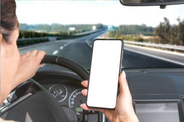 Araba kullanırken elinde boş cep telefonu olan bir kadın. Araba otoyol boyunca hız yapıyor. Araba kullanırken mesaj yazma. Arabada oturan ve akıllı telefon kullanan bir kadın. Telefon ekranı ile ayarla
