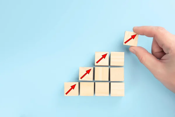 concept of revenue growth. growth on stacked wooden cubes on blue background. Financial or business growth concept. arrows icons on wooden cubes. Hand putting wooden cube block on top