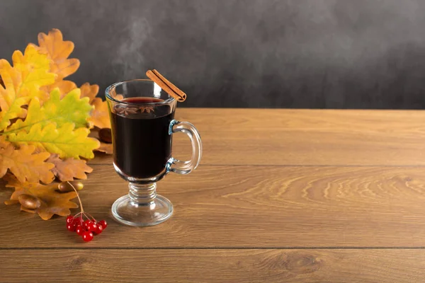 mulled wine and autumn fallen leaves. still life a mug of Mulled wine with spices against the background of fallen oak leaves. Cup of hot wine with, spices and autumnal leaves on old rustic wooden background, autumn concept. copyspace