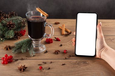 Kış yılbaşı süslemelerinin arka planında beyaz ekranlı bir kadının elinde modern cep telefonu. Yılbaşı model telefonu.