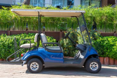 Turist otelinde küçük bir golf elektrikli arabası. Yeşil arka planda yol kenarına park edilmiş mavi elektrikli araba.