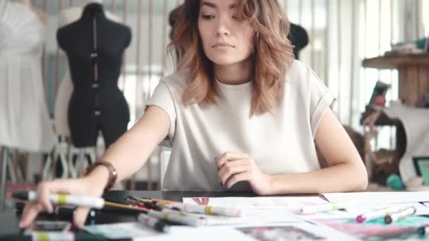 Модный дизайнер делает эскиз на бумаге и отправляет сообщение с мобильного телефона. деловая женщина, работающая в своем ателье — стоковое видео