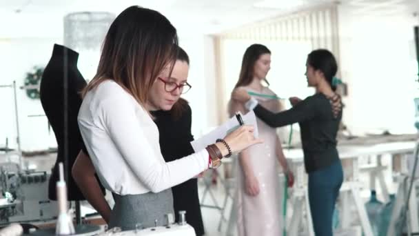 Gruppo di sarti lavorano nell'atelier. giovane donna alla moda designer parla con il suo assistente e guarda lo schizzo dei vestiti — Video Stock