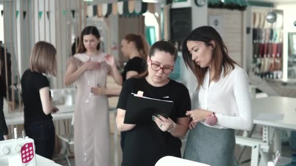 Eine Gruppe von Schneiderinnen arbeitet an einem neuen Kleidungsmodell. Näherinnen kümmern sich um die Passform des Kleides. junge Modedesignerin und ihr Assistent diskutieren im Atelier — Stockvideo