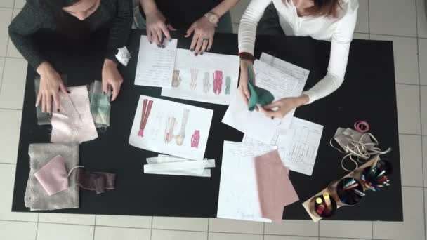 Moda tasarımcıları bir grup skeçler giysi tartışmak ve terzilik için bir kumaş seçin. Terziler atelier içinde. üstten görünüm — Stok video