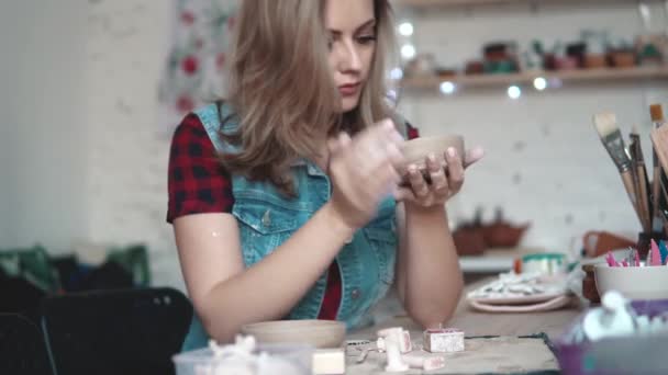 Молодая женщина создает тарелку глины в мастерской. Девушка держит в руках форму глины. the creative hobby — стоковое видео