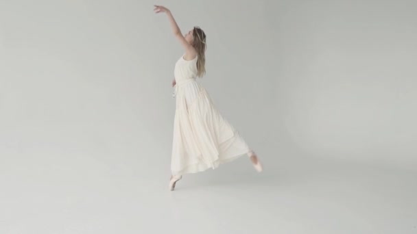 Une gracieuse ballerine vêtue d'une robe légère danse sur les orteils en pointes. danseuse de ballet dansant sur fond blanc. au ralenti — Video