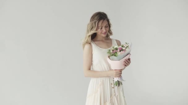 Портрет нежной молодой девушки с букетом цветов. блондинка в бежевом платье на светлом фоне — стоковое видео