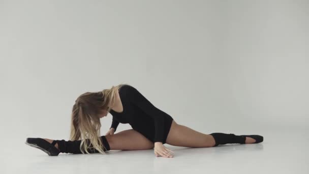 Eine schlanke Ballerina beim Stretching, sitzend auf einem Bindfaden auf dem Boden. Turnerin in schwarzem Body und Leggings — Stockvideo