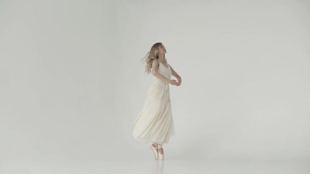 Un retrato suave de una joven bailarina con un vestido ligero y puntas beige. bailarina de ballet bailando sobre fondo blanco — Vídeo de stock