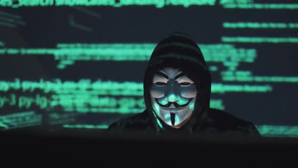 Räuber im Hintergrund läuft Programmcode. Hacker in der Maske hackt das Programm. die digitale Erpressung erhält Zugang zu Informationen anderer Völker. Computervirus-Angriff — Stockvideo