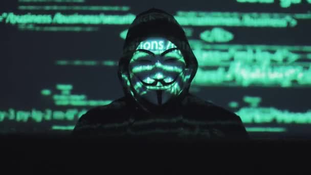 Anónimo en la máscara roba datos de usuario en la red. hacker contra el fondo del código en ejecución — Vídeo de stock
