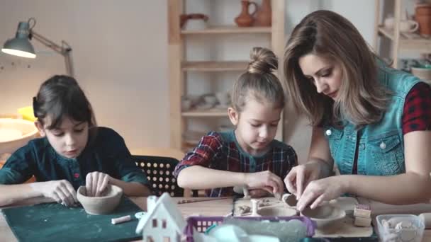 Eine junge Mutter mit zwei kleinen Töchtern beschäftigt sich in einer Heimwerkstatt mit Kreativität. Kinder basteln aus Ton — Stockvideo