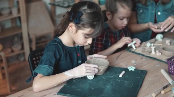 Uma menina está fazendo um artesanato de barro em uma oficina de cerâmica. Mãe e criança passam tempo juntos fazendo trabalho criativo — Vídeo de Stock